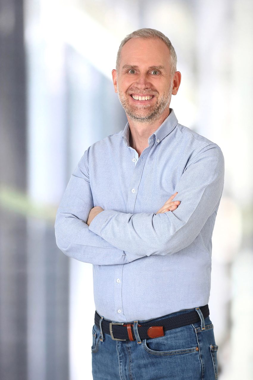 Johannes Geyer smiling with arms crossed, wearing a light blue shirt